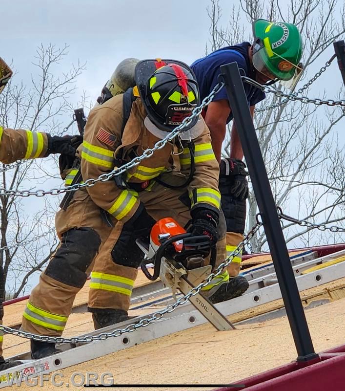 WGFC firefighter demonstrates opening up a roof with a saw under the watchful eyes of an instructor. 